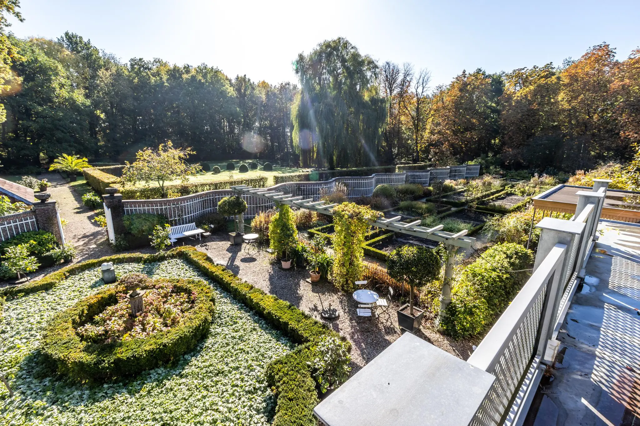Zonnige overzichtsfoto van een formele tuin aan de Langbroekerdijk, omgeven door groen en sierhekken.